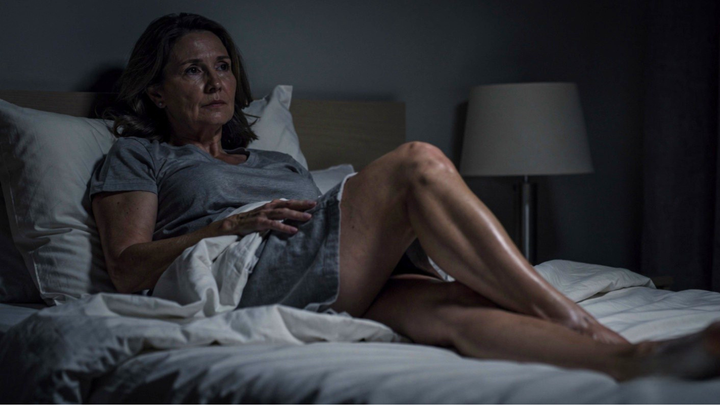Restless legs in menopause: woman lying awake in bed at night with legs uncovered, unable to sleep