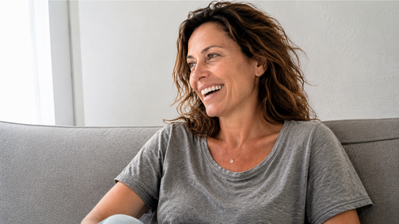 Woman sitting on a couch, smiling, with a neutral background