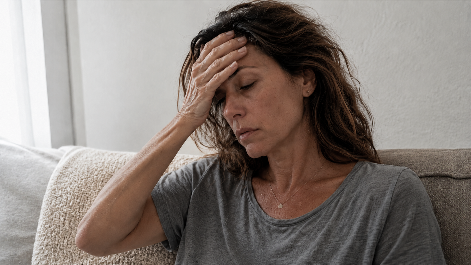 Woman sitting on a couch with her hand on her head, appearing stressed or tired.