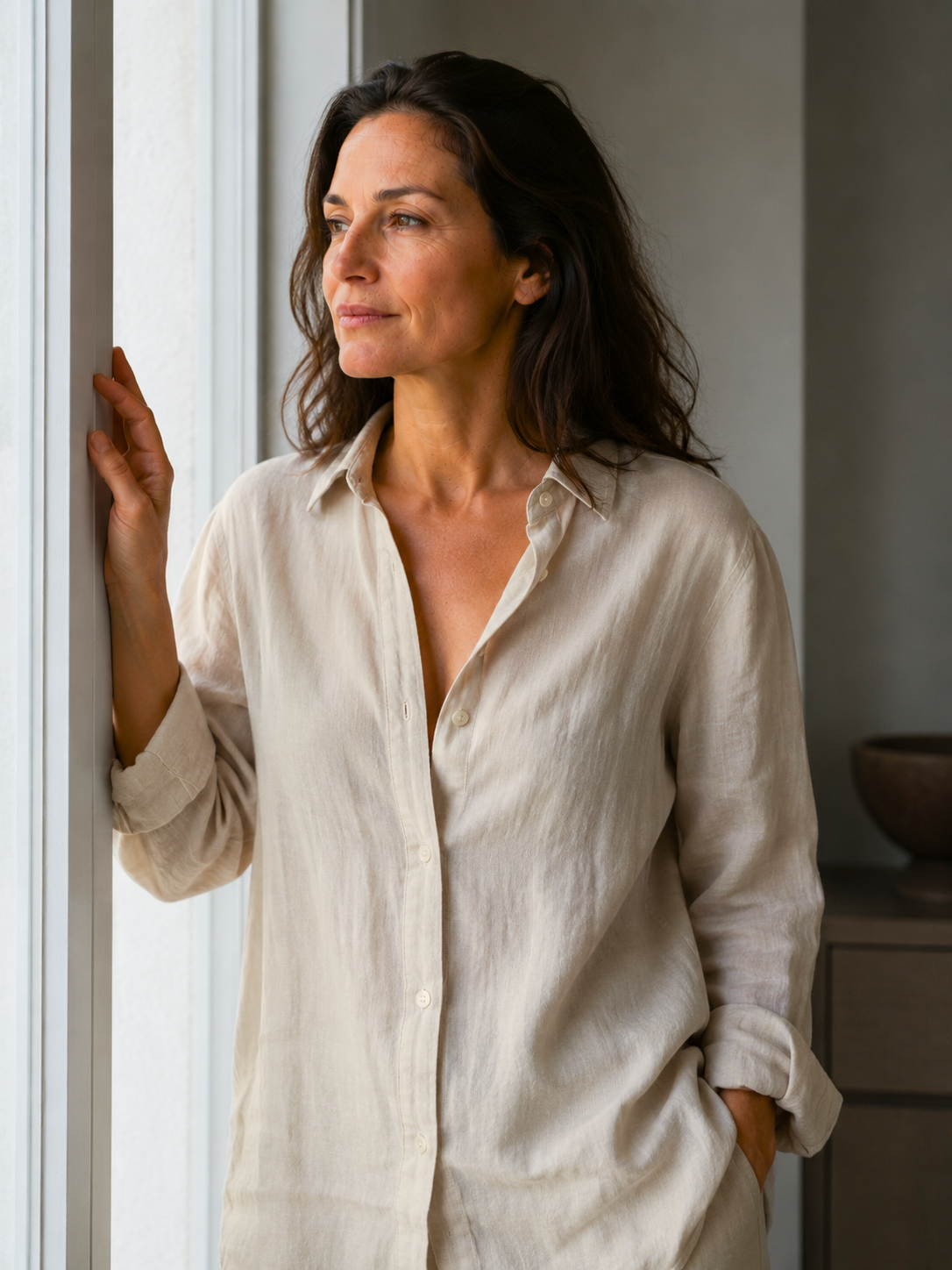 Woman in a beige shirt standing by a window