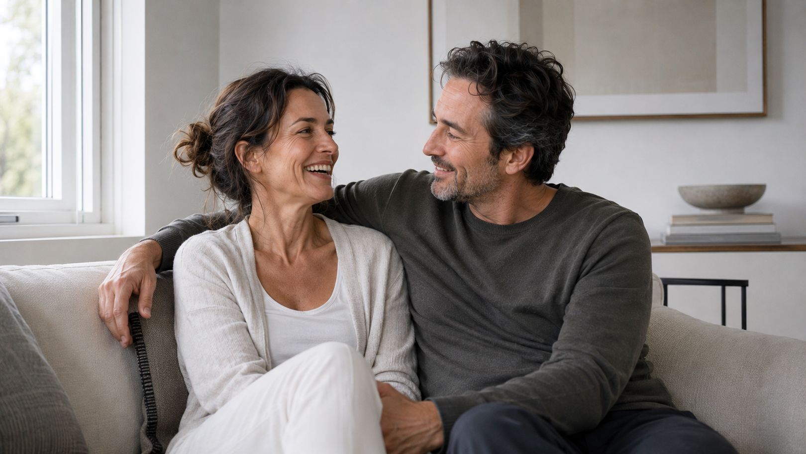 Man and woman sitting on a couch, smiling at each other in a home setting